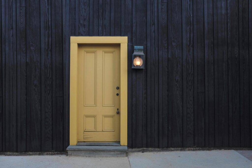 A modern yellow door on a dark wooden facade creates a striking contrast. Architectural detail.
